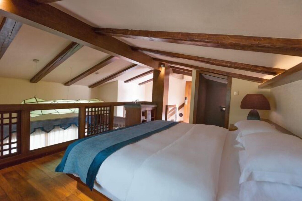 A bedroom with a bed, wooden beams, a window, and a door.