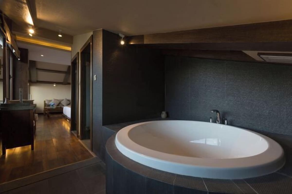 A modern bathroom with a large oval bathtub, dark walls, and a wooden floor.