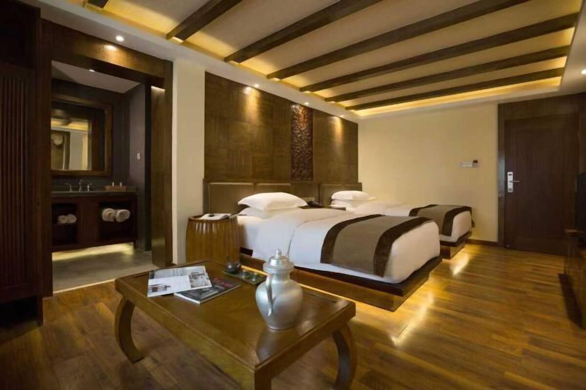 Ein Hotelzimmer mit Holzboden, zwei Betten, einem Nachttisch mit einer Vase und einer Holzzieldecke.