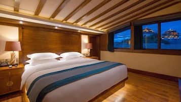 Habitación de hotel con una cama grande, vigas de madera en el techo, dos lámparas de noche y vista a un edificio al otro lado del agua.