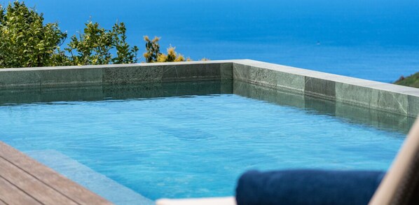 A swimming pool with a wooden deck and a view of the ocean.