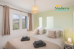 Quarto com cama, duas janelas, vista para a paisagem, luminária pendente e um logotipo na parede.