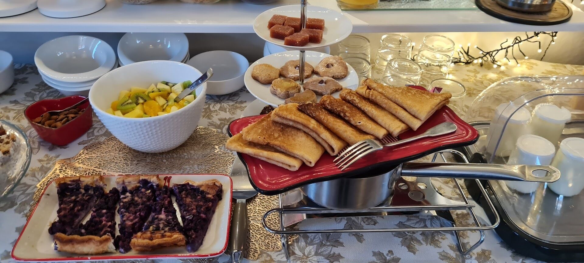 Uma mesa de buffet com diversos pratos, incluindo torta, salada de frutas, doces e um prato vermelho com rolinhos.