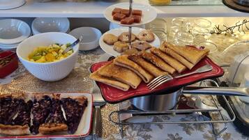 Uma mesa de buffet com diversos pratos, incluindo torta, salada de frutas, doces e um prato vermelho com rolinhos.