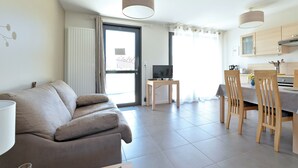Un salon moderne comprenant un canapé, une table à manger avec des chaises, un téléviseur et un coin cuisine.