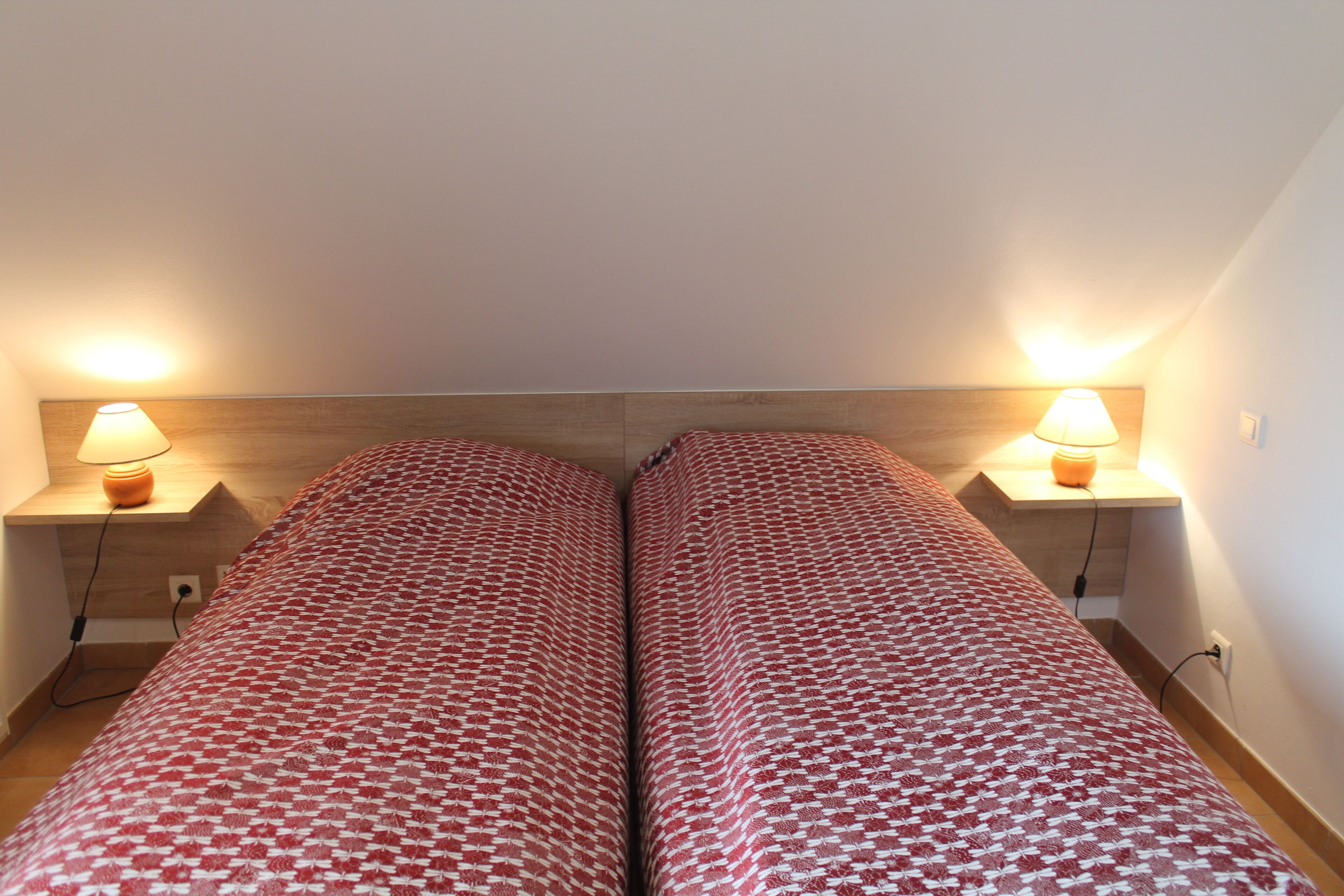 Une chambre double avec deux lits, chacun agrémenté d’une couvre-lit à motifs, de lampes de chevet et d’une tête de lit en bois.