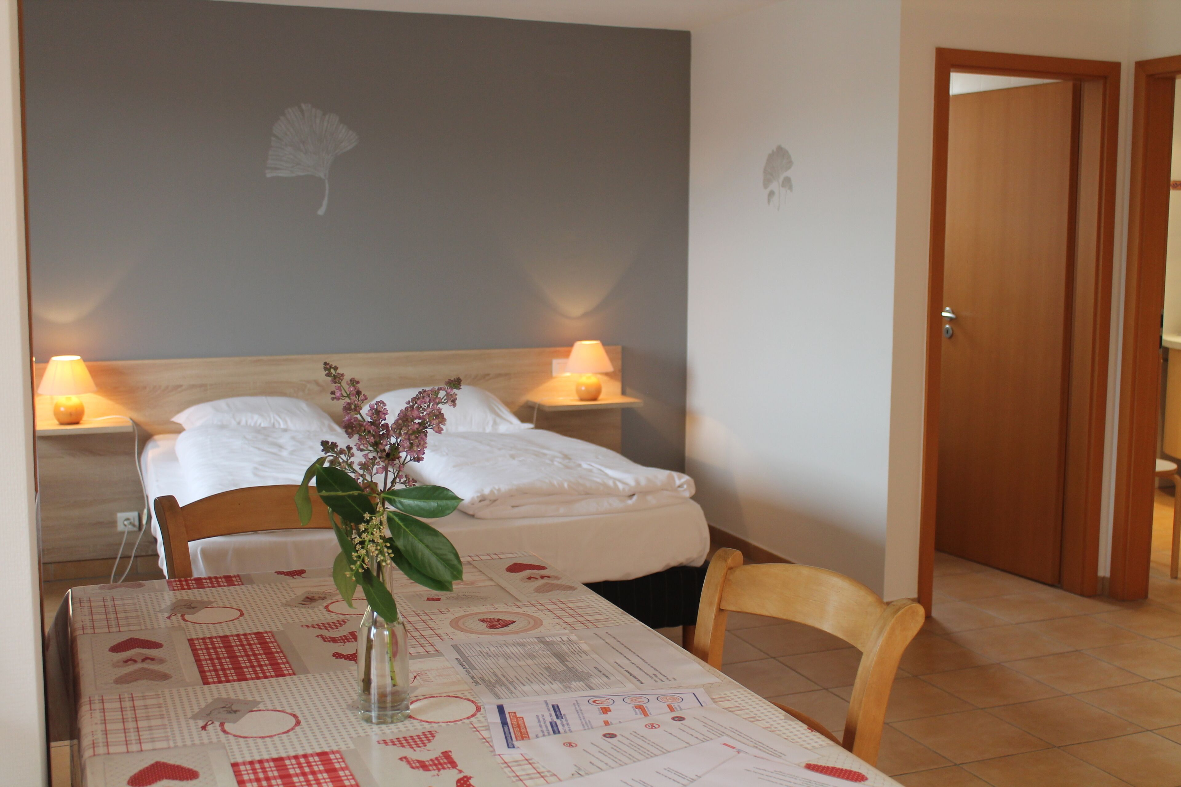 Una camera d'albergo con un letto, lampade sui comodini, un tavolo con un centrotavola floreale e una sedia.