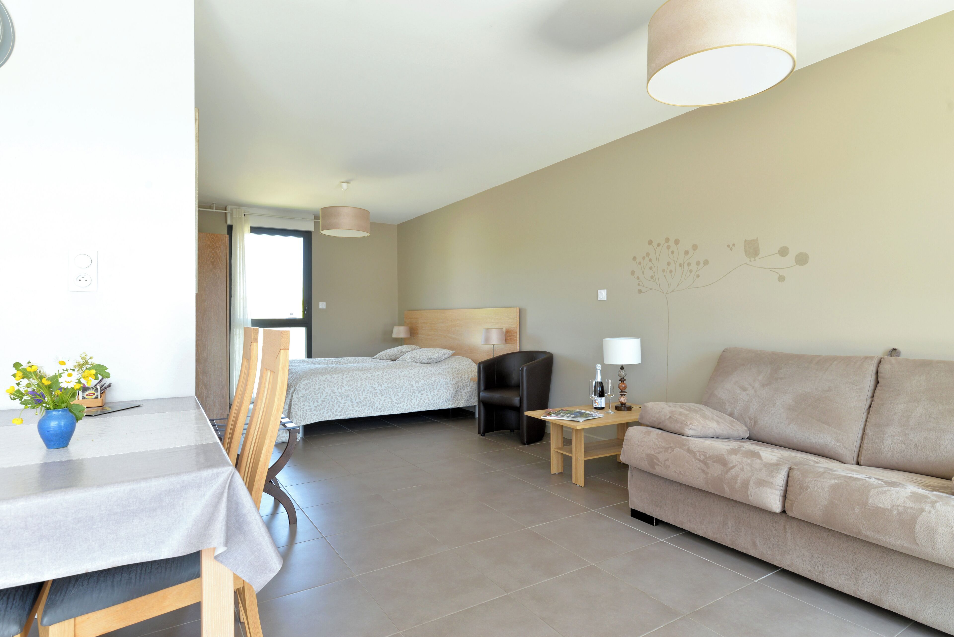 Une chambre d’hôtel comprenant un lit, un canapé, une table à manger avec des chaises, une lampe et un vase avec des fleurs.