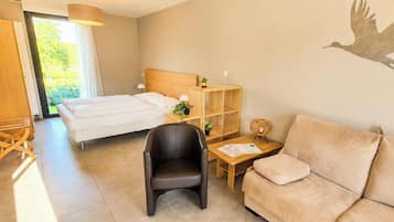 Hotelkamer met een bed, een houten nachtkastje, een zwarte stoel, een beige bank en een muurschildering.