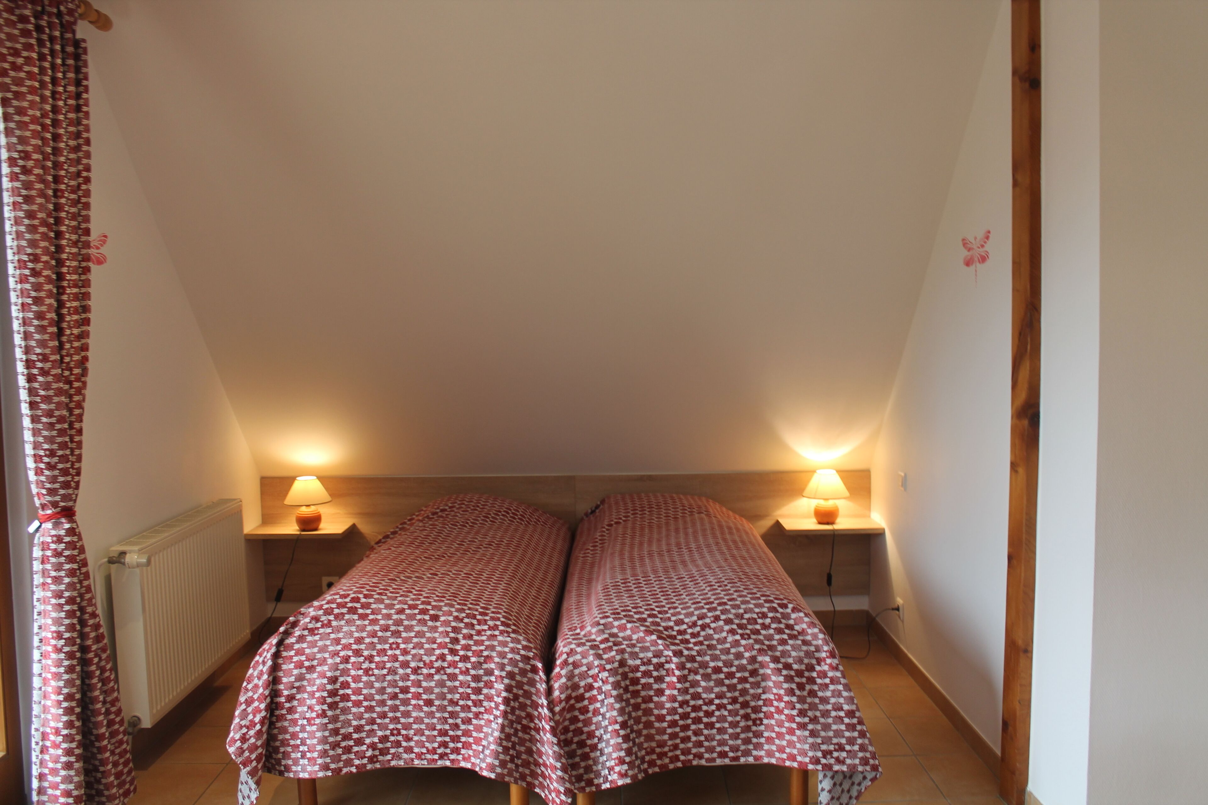 Una habitación pequeña y acogedora con dos camas cubiertas con ropa de cama estampada, un radiador y dos lámparas de noche.