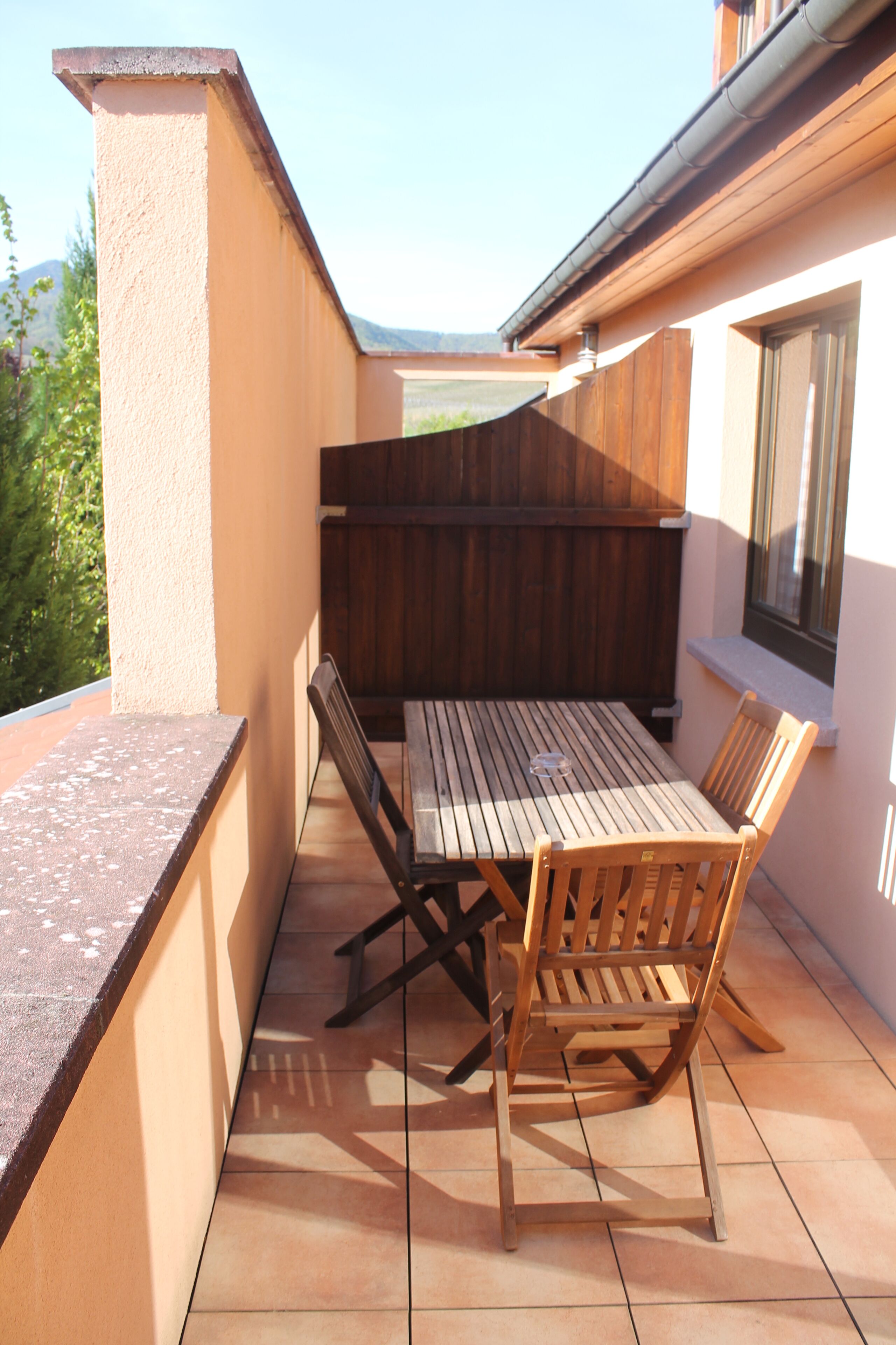 Une terrasse avec une table et des chaises en bois, une fenêtre et une clôture en bois.
