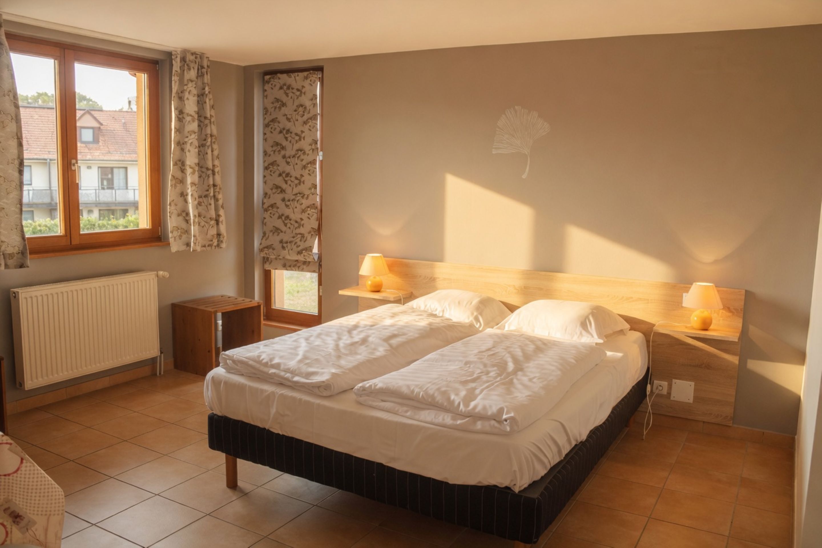 Een slaapkamer met een tweepersoonsbed, bedlampen, een radiator, een raam met gordijnen en een ventilator aan de muur.
