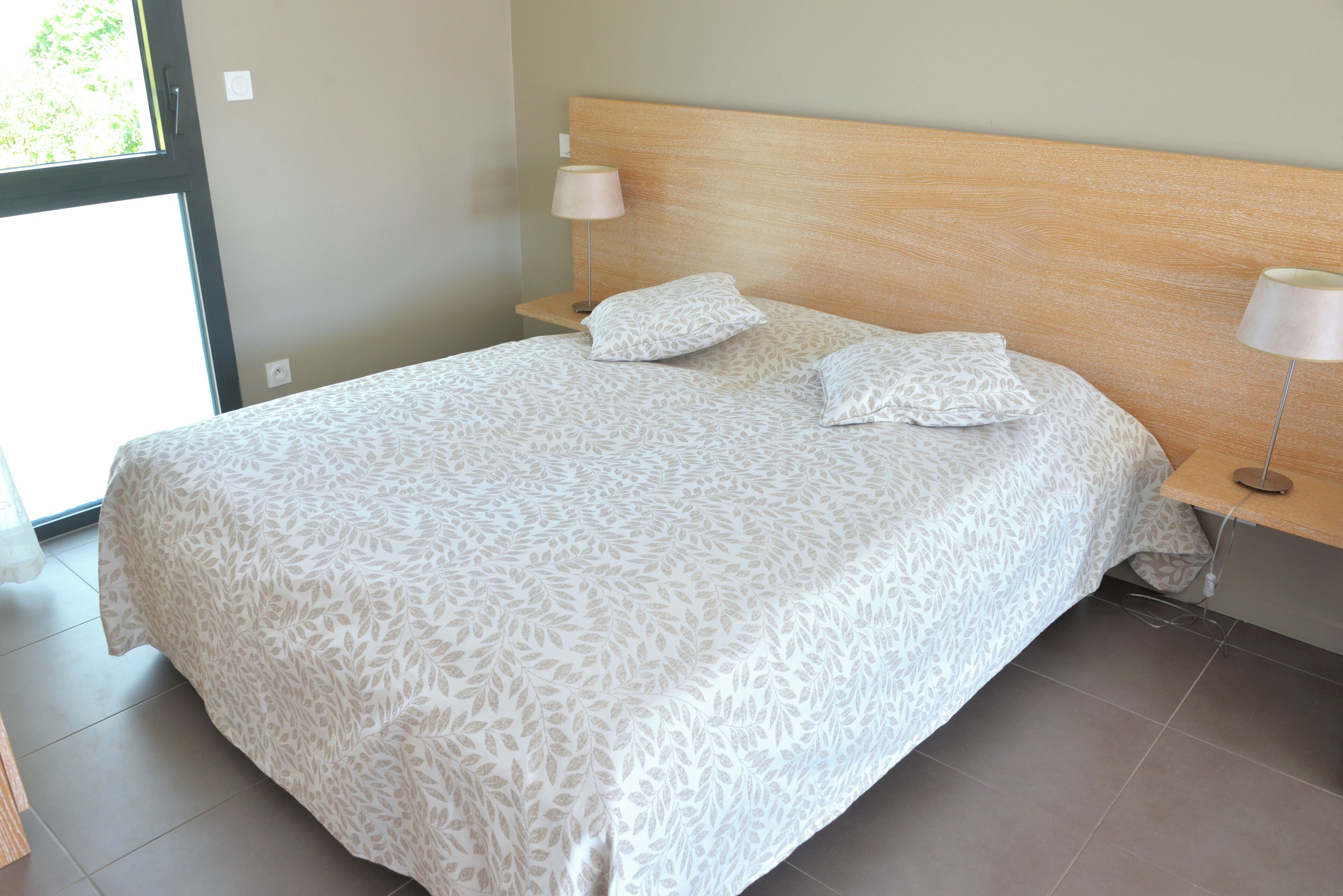 A neatly made bed with a patterned bedspread, a wooden headboard, and two bedside lamps.