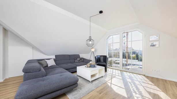 Un soggiorno moderno in stile loft con un divano componibile, un tavolino bianco e un'ampia finestra con vista sulla città.