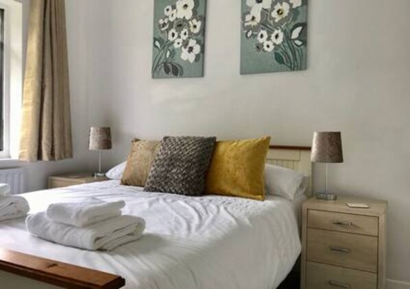 A neatly made bed with white linens, a bedside lamp, and a nightstand with a lamp.