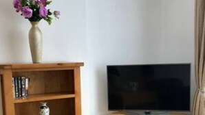 A wooden TV stand with a flat-screen TV, a small shelf with books, and a vase with flowers on top.