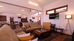 A spacious living room with a large sofa, a coffee table, and a television mounted on the wall. - The Forest Haven  (Ooty)