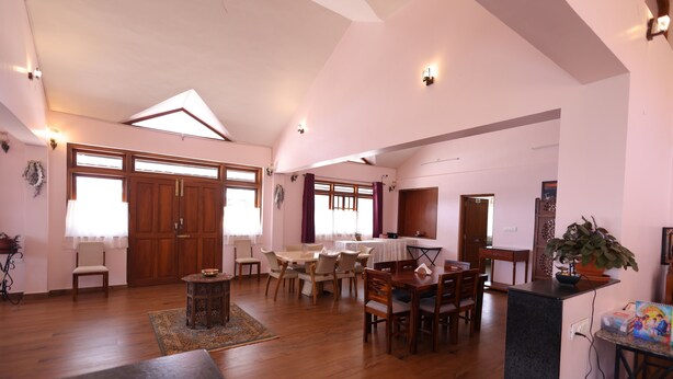 A spacious living area with a high ceiling, wooden flooring, and a dining area with multiple chairs and a table. - The Forest Haven  (Ooty)