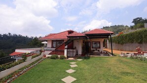 A two-story house with a red-tiled roof, a covered porch, and a well-maintained lawn with stepping stones. - The Forest Haven  (Ooty)