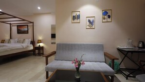 A hotel room with a bed, a sofa, a coffee table with a vase of flowers, and a small table with a lamp. - The Forest Haven  (Ooty)