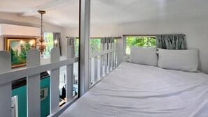 A bedroom with a bed, white curtains, a window with a view of greenery, and a ceiling fan. - Treehouse with golf cart in Shepherd - near Lake with wild alligators (Shepherd)