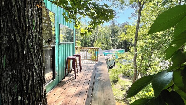 A wooden deck with a glass door, a red tactile paving, and a view of a green building and trees. - Treehouse with golf cart in Shepherd - near Lake with wild alligators (Shepherd)