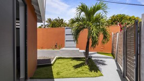 Ein schmaler Innenhof mit einer Palme, einer kleinen Rasenfläche und einem Betonweg, der zu einem Tor führt.