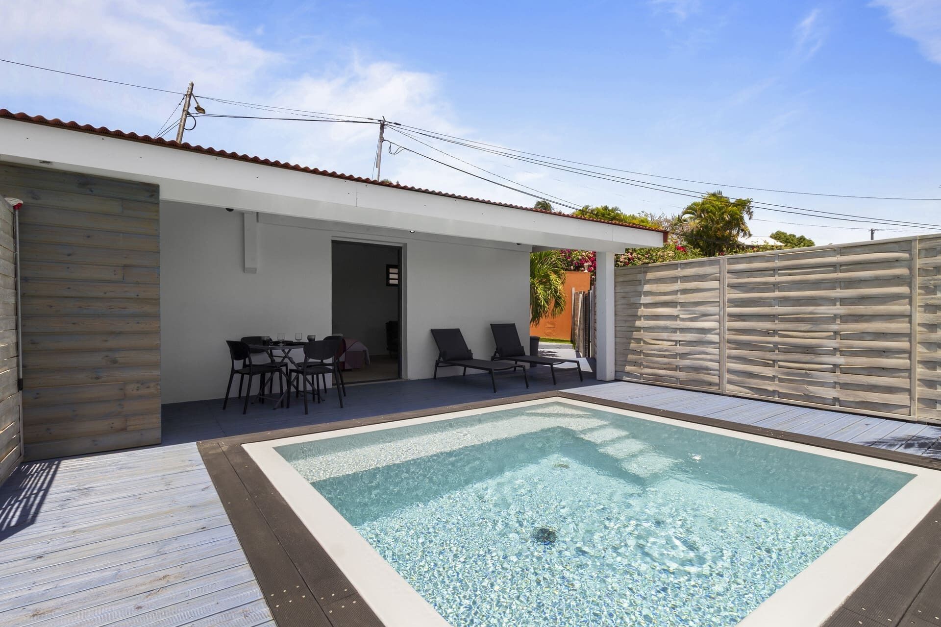 A swimming pool area with a wooden deck, lounge chairs, and a covered seating area.