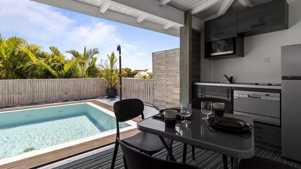 Eine moderne Außenküche mit Pool, Essbereich und Blick ins umgebende Grün.