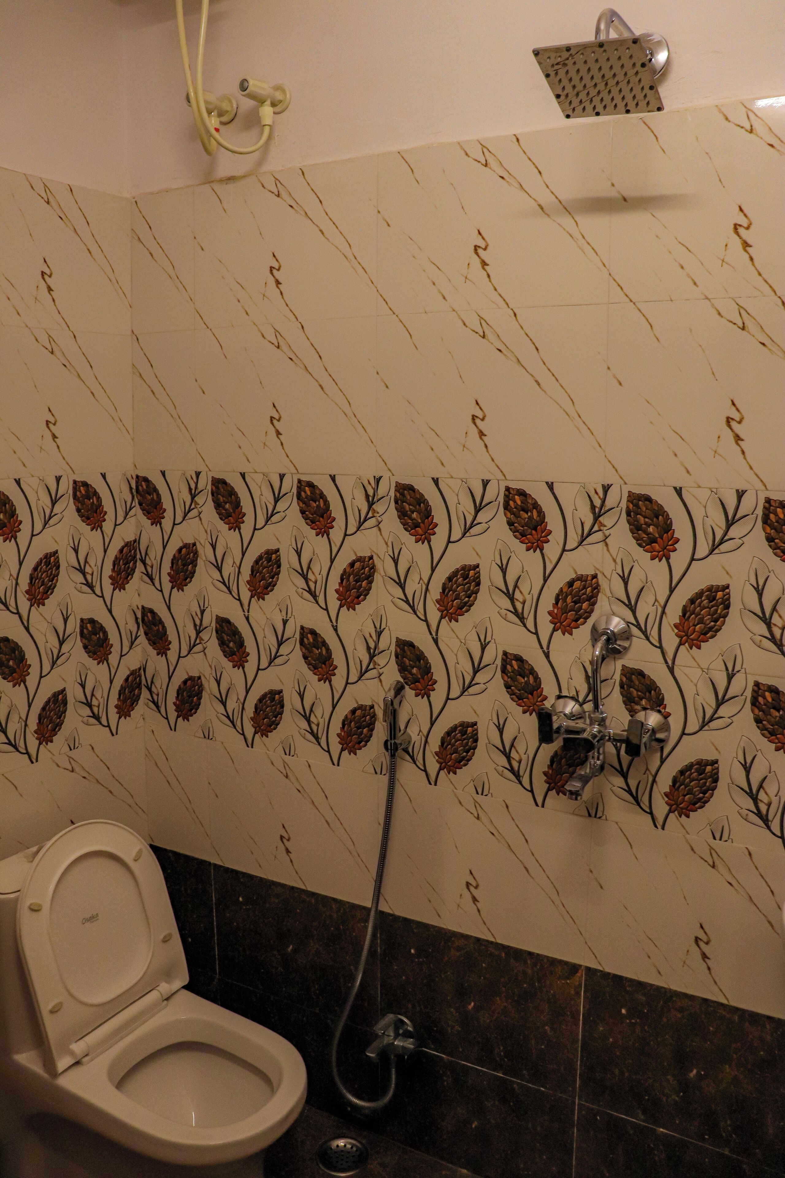 Un baño con inodoro, ducha y una pared con diseño de hojas.