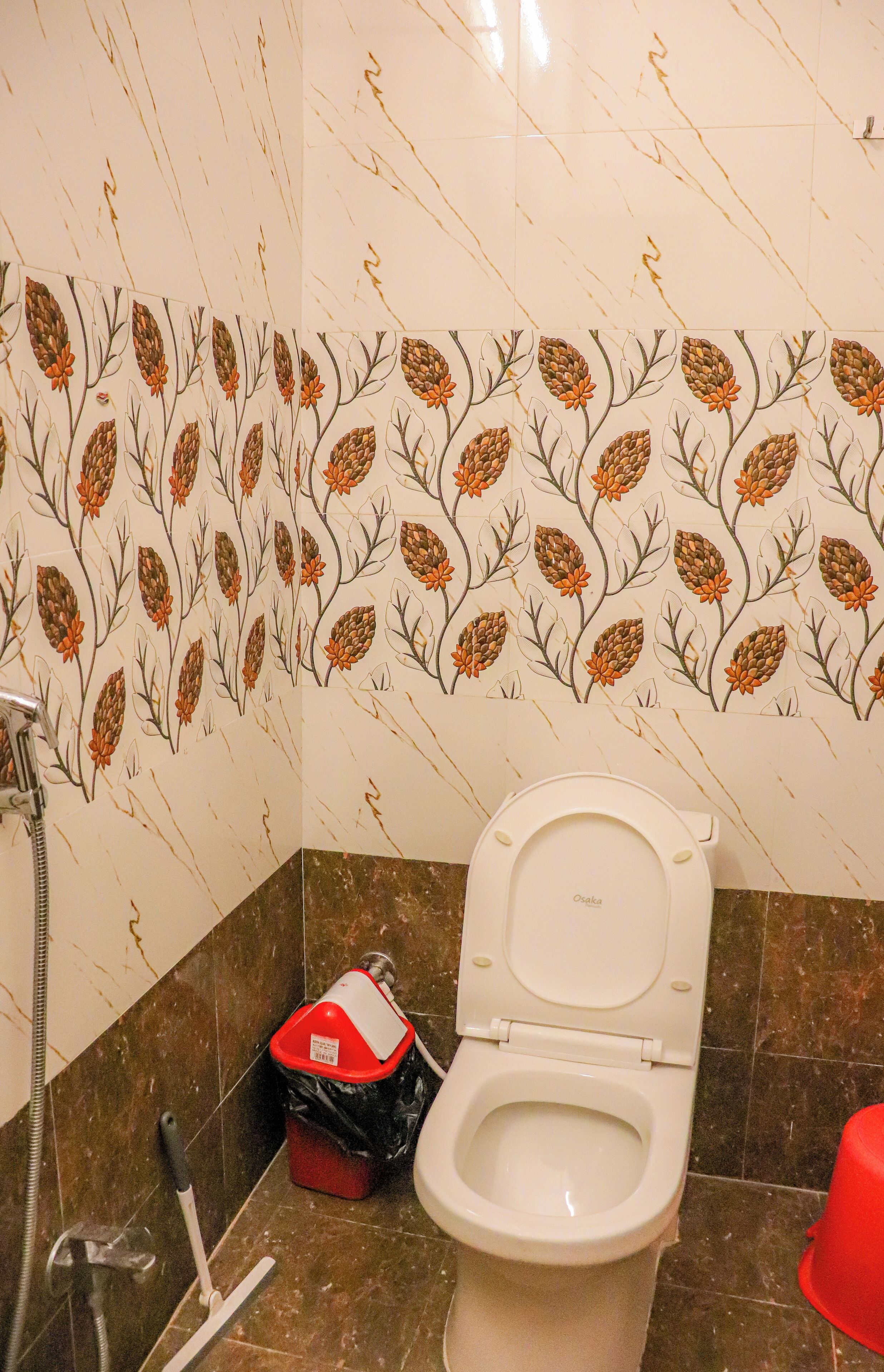 A bathroom with a toilet, a red trash bin, and a shower hose.