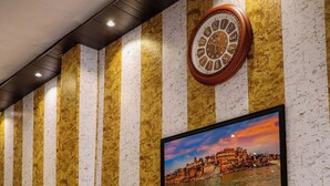 Un vestíbulo de hotel con una zona de estar con banca de madera, un reloj y un cuadro en la pared.