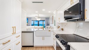 Cocina moderna con armarios blancos, pomos dorados, estufa negra y un amplio ventanal con vistas a un balcón.