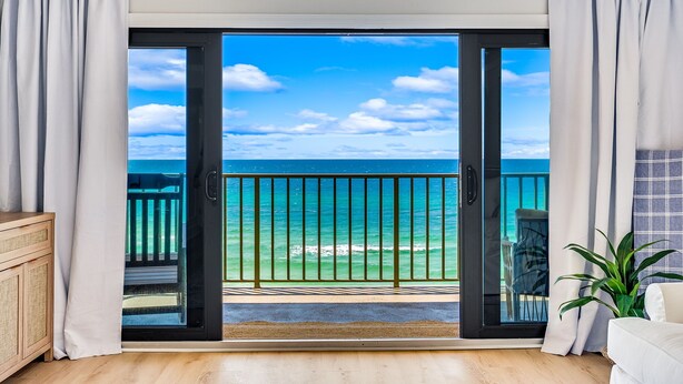 Una habitación con puerta de vidrio corredera que da a un balcón con vista al océano.