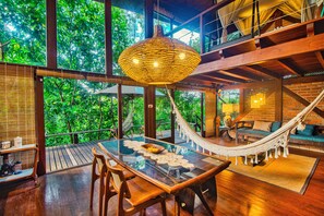 A spacious room with a large glass table, wooden chairs, a hammock, and a view of lush greenery through large windows. - ascasinhaZ Morro de São Paulo (Gamboa)