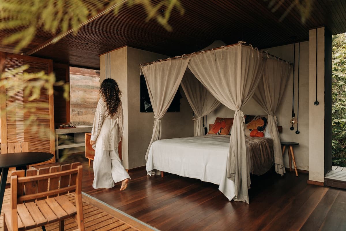 A bedroom with a canopy bed, wooden flooring, and a small table with chairs.