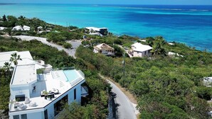 A modern house with a swimming pool, surrounded by lush greenery and a clear view of the ocean. - GardenSuite at Aqualara Villa w/ shared Rooftop Infinity Lounge Pool & Patio (Providenciales)