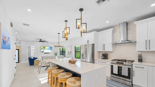 A modern kitchen with white cabinets, a large island with stools, stainless steel appliances, and pendant lighting.