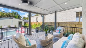 A covered outdoor patio with wicker furniture, a pool, and a view of the surrounding area.
