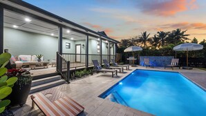 A modern outdoor pool area with lounge chairs, a covered seating area, and a staircase leading to a covered patio.