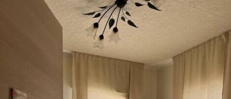 Une chambre d’hôtel avec un lit, une chaise, un téléviseur fixé au mur et une fenêtre avec des rideaux.