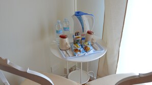 Et spiseområde med to hvide stole og et lille bord, en elkedel samt en bakke med mad og drikke.
