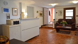 En stue med en brun sofa, et sofabord og et spisebord med stole. Der er også et køkkenområde med et køleskab og en mikrobølgeovn.