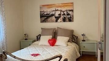 A bedroom with a bed, a nightstand, a bedside table, a painting on the wall, and a chandelier.