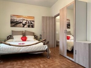 Een slaapkamer met een bed, een houten kledingkast, een spiegel en een schilderij aan de muur.