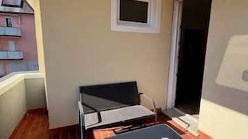 Een klein balkon met een tafel, een bank, een raam en een deur.