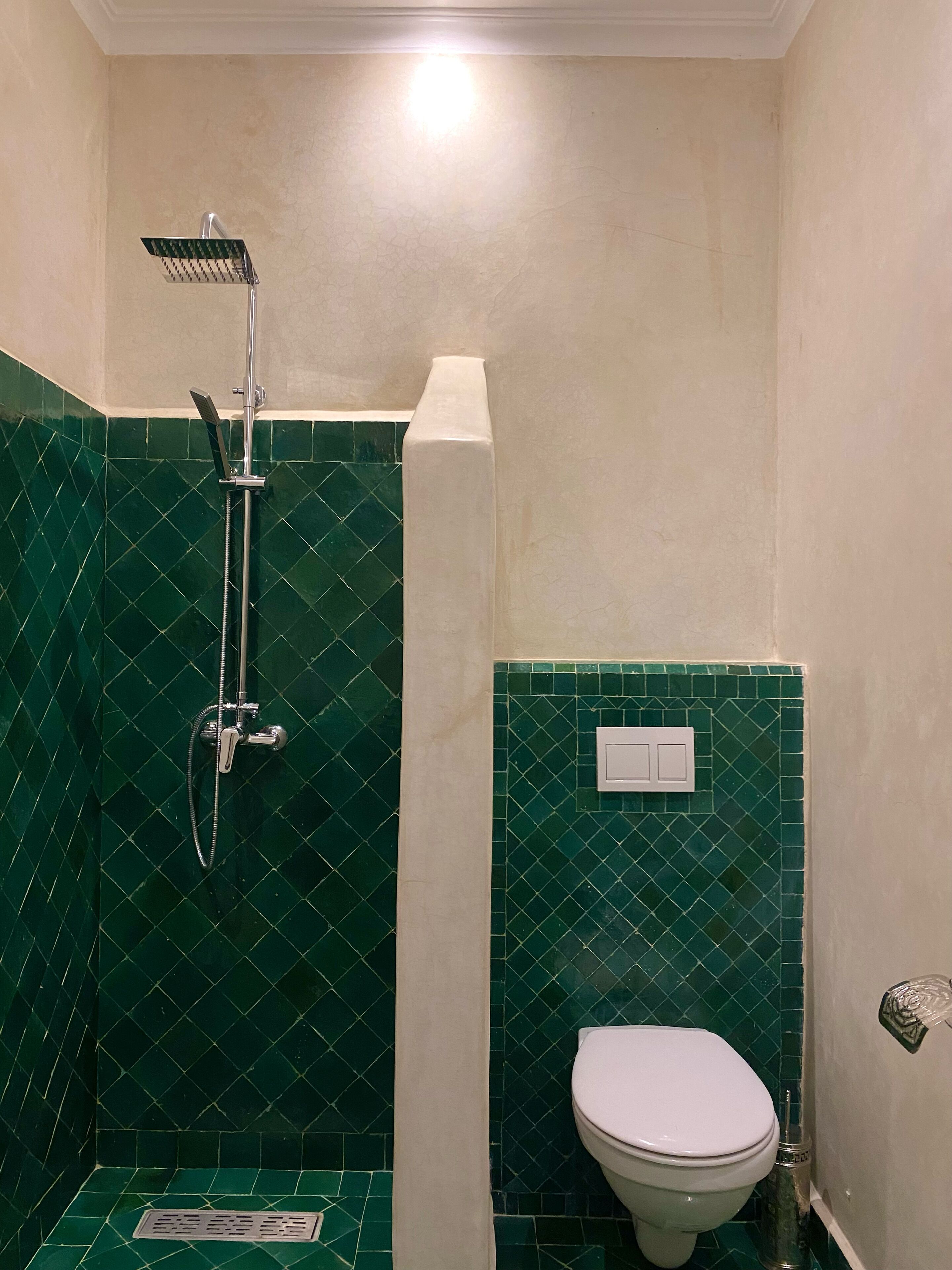 Et lille badeværelse med bruser, toilet og vægge med grønne fliser.