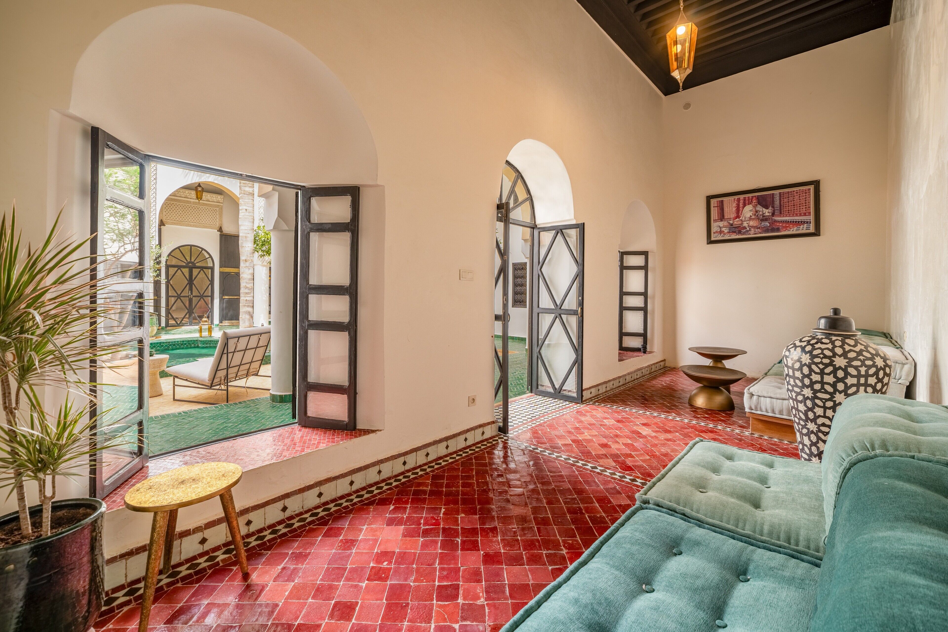 A spacious living area with a red tiled floor, a green sofa, a small round table, and a potted plant.