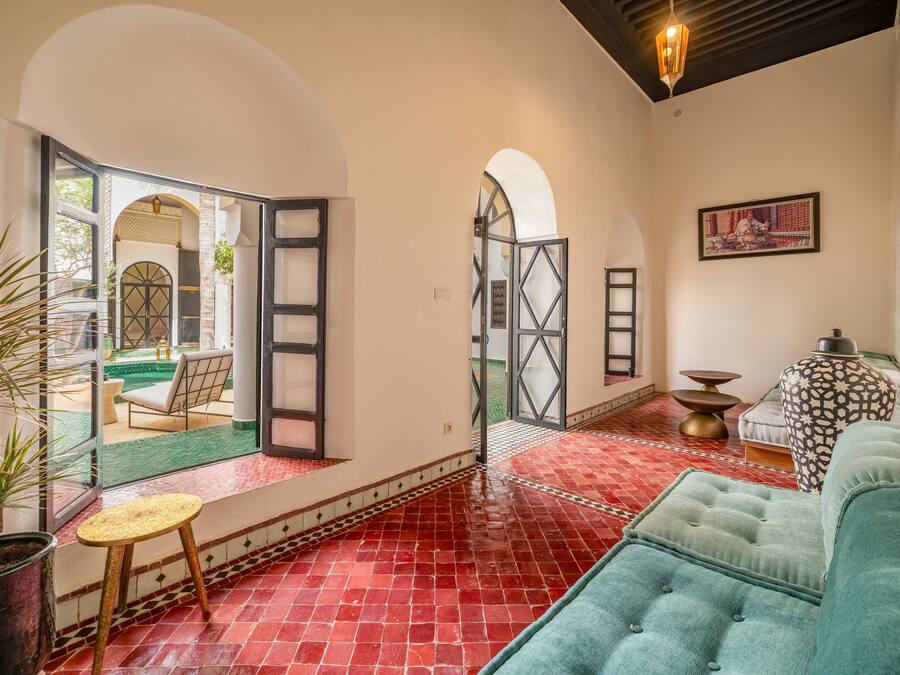 A spacious living area with a red tiled floor, a green sofa, a small round table, and a potted plant.