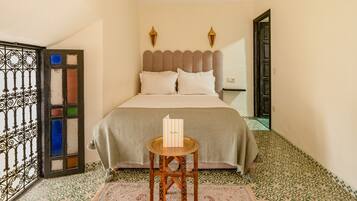 Un dormitorio con cama, una mesita con un cartel, baldosas de suelo con diseño y una puerta decorativa.